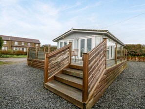 A wooden staircase leading to a covered outdoor area with a chair and a table. - Caban Tywod (Pwllheli)