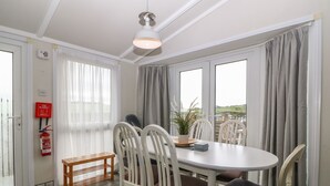 A dining area with a round table, white chairs, a small wooden bench, and a potted plant. - Caban Tywod (Pwllheli)