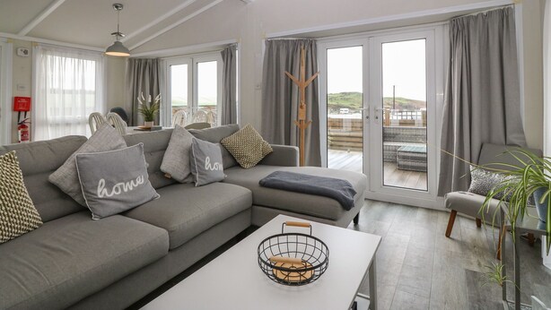 A modern living room with a grey sofa, a white coffee table, and a balcony with grey curtains. - Caban Tywod (Pwllheli)