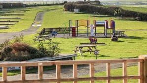 A playground with a slide and climbing structures, picnic tables, and a speed limit sign. - Caban Tywod (Pwllheli)