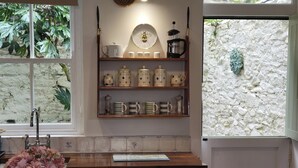 Una cocina con cafetera, tetera y tazas sobre estantes, un lavamanos y lavavajillas.