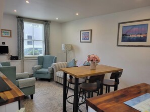 Ein gemütliches Wohnzimmer mit einer Couch, einem Esstisch mit Stühlen, einer Lampe und gerahmten Bildern an den Wänden.
