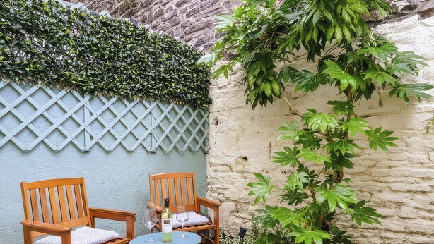 Un patio con dos sillas de madera, una mesa redonda pequeña y una botella de vino.