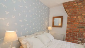 Ein Schlafzimmer mit einem Bett, zwei Nachttischen, einer Lampe, einem Spiegel und einer Ziegelwand.
