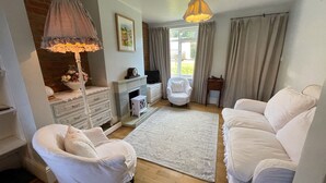 Ein gemütliches Wohnzimmer mit Kamin, weißen Möbeln, einer Deckenleuchte und Blick ins Freie.