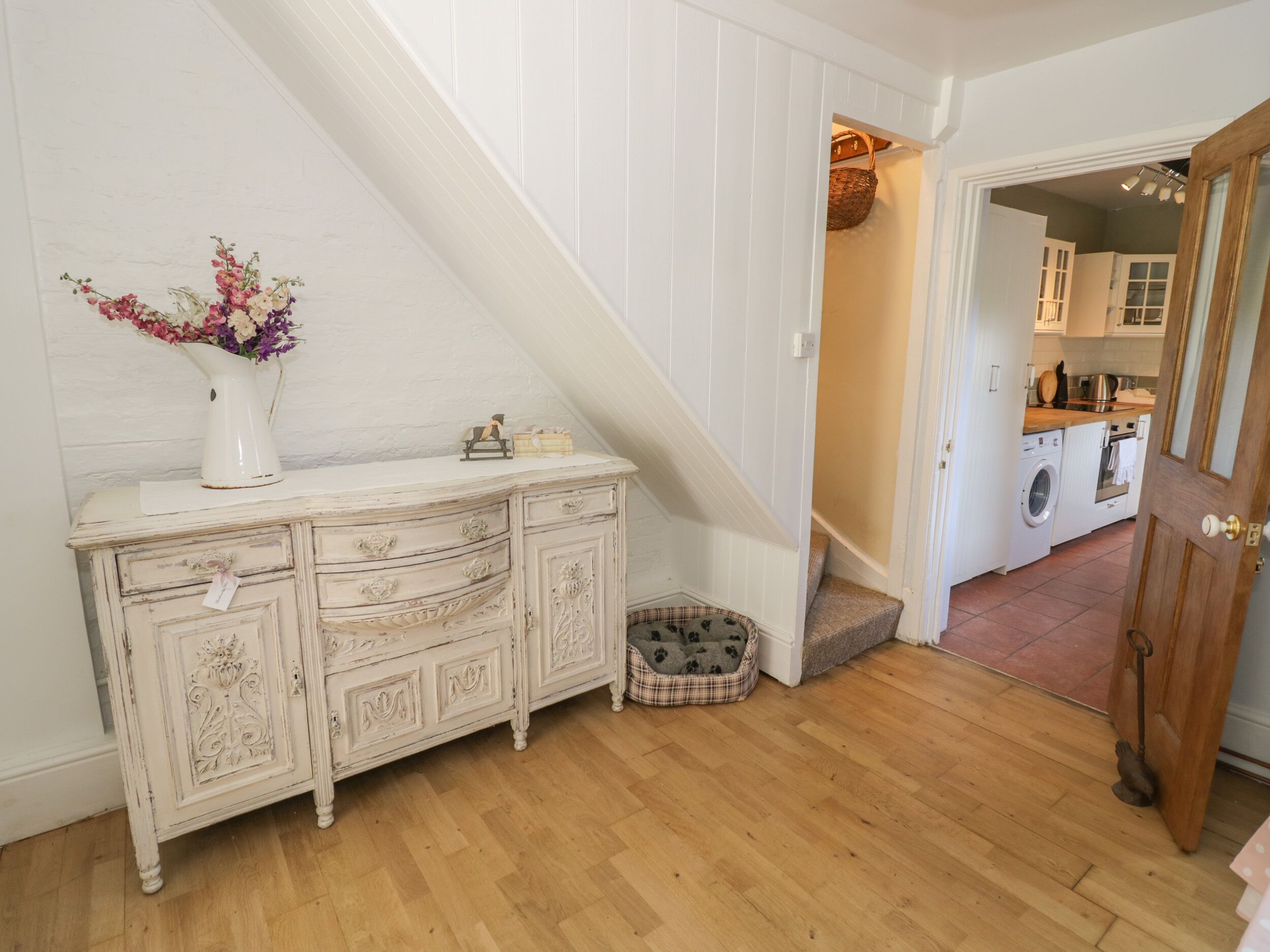 A staircase leading to a laundry area with a white dresser and a pet bed.