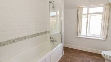 A bathroom with a bathtub, a shower, a toilet, and a window.