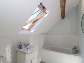 Un baño moderno con tragaluz, una bañera independiente y un tocador blanco.
