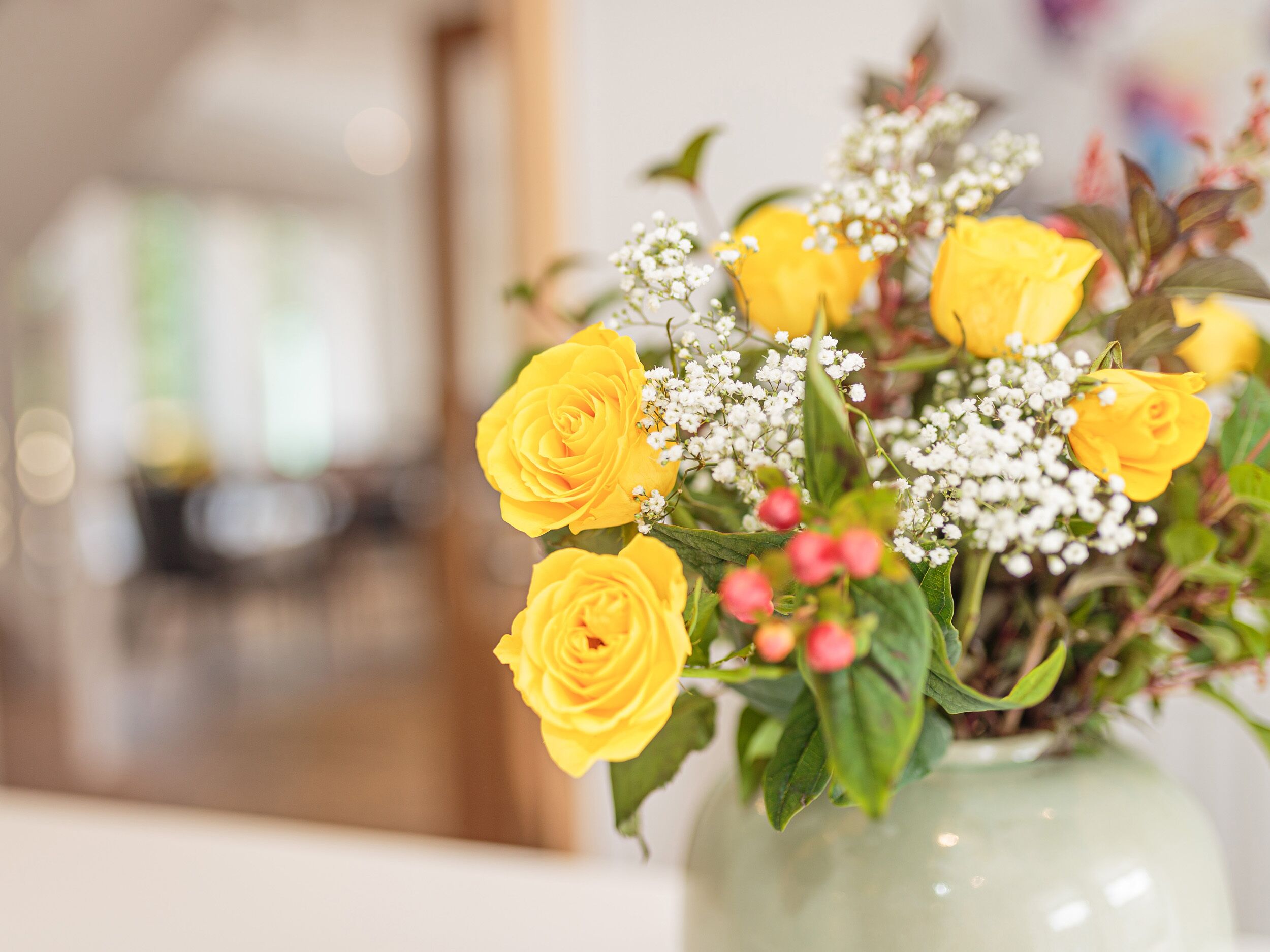 A bouquet of yellow roses and baby's breath in a clear glass vase.