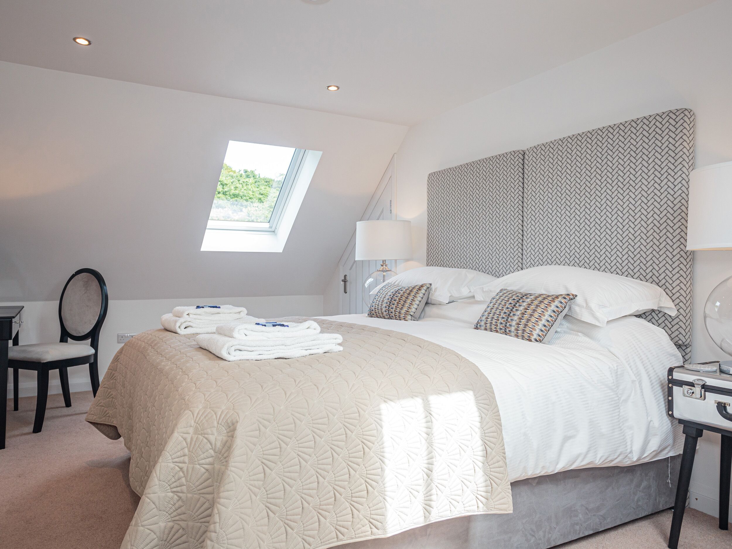 A modern hotel room with a large bed, a desk, a chair, and a skylight.