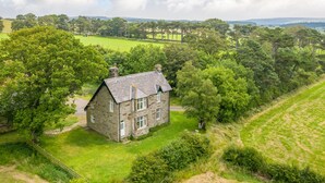 Une maison en pierre, dotée d’un toit en pente, entourée d’une végétation luxuriante et de champs.