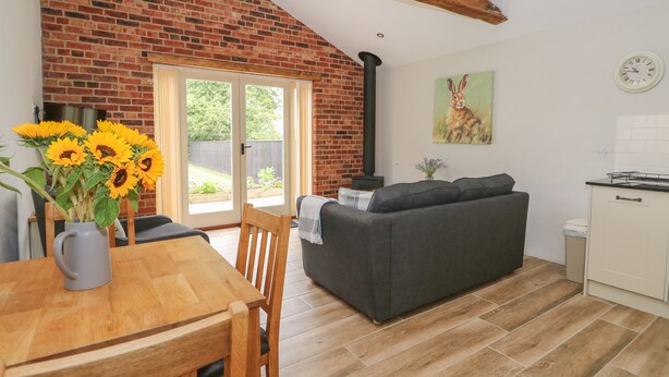 A cozy living room with a fireplace, a dining area with a wooden table and chairs, and a kitchen with a white cabinet. - Sunrise Stable (Spalding)
