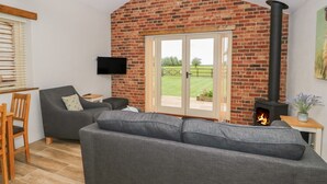A cozy living room with a brick fireplace, a grey sofa, and a television mounted on the wall. - Sunrise Stable (Spalding)