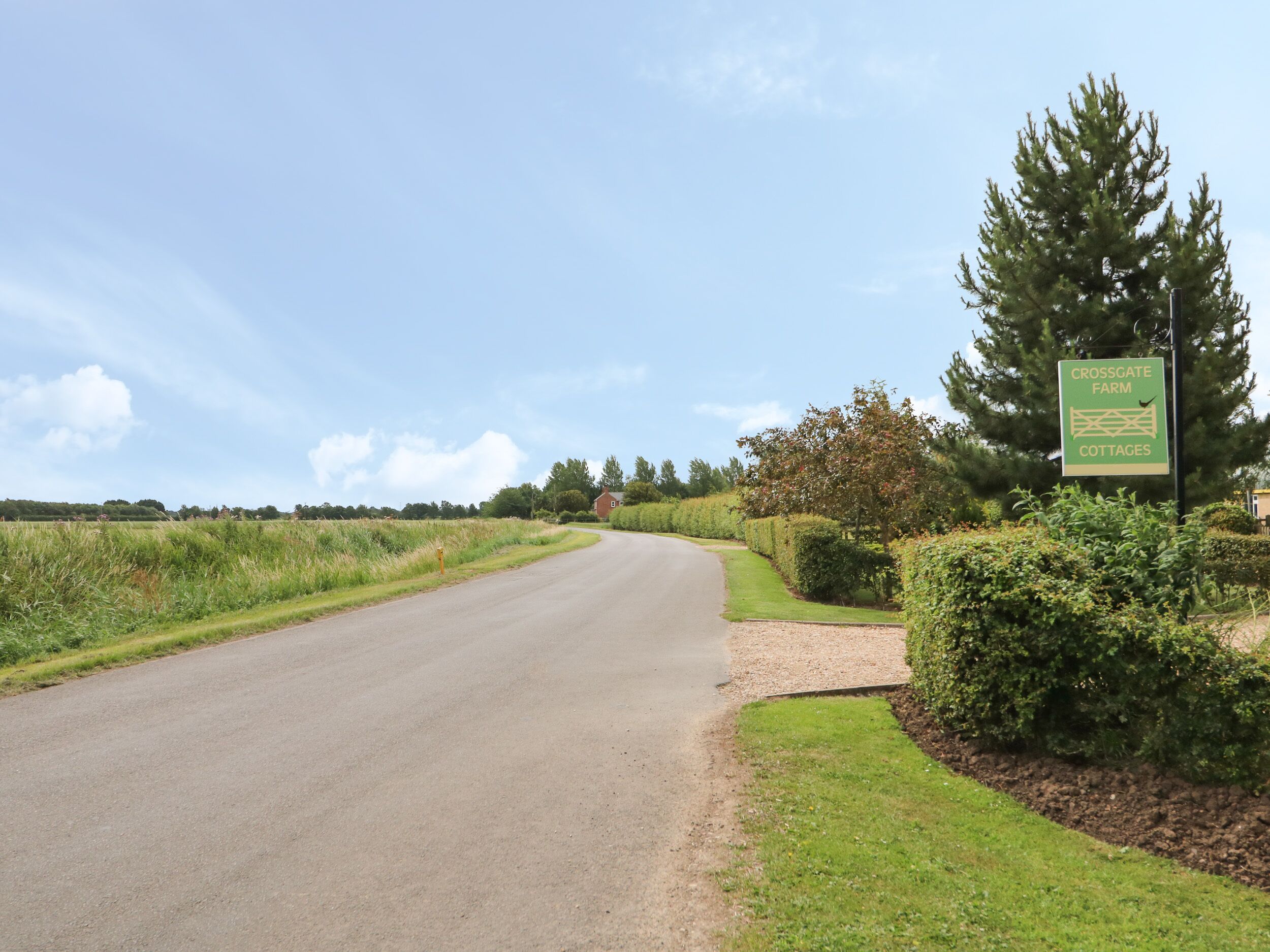 Une route de campagne avec un panneau indiquant « Crossgate Farm Cottages ».