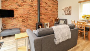 Una sala de estar acogedora con pared de ladrillo, chimenea, sofá gris, mesa de comedor de madera y televisor montado en la pared.