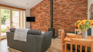 Una sala de estar moderna con pared de ladrillo, chimenea, sofá, televisor y comedor con mesa y sillas.