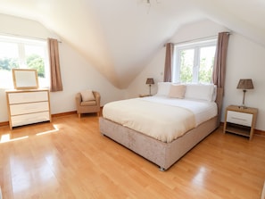 A bedroom with a large bed, a dresser, a chair, and a nightstand with lamps.