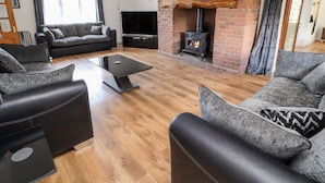 A modern living room with a brick fireplace, a flat-screen TV, and grey upholstered sofas. - Bryn Awel (Denbigh)