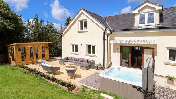 A two-story house with a patio area, a hot tub, and a wooden cabin-like structure. - Bryn Awel (Denbigh)
