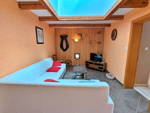 A cozy room with a white sofa, a small table, a TV, wooden walls, and a skylight.