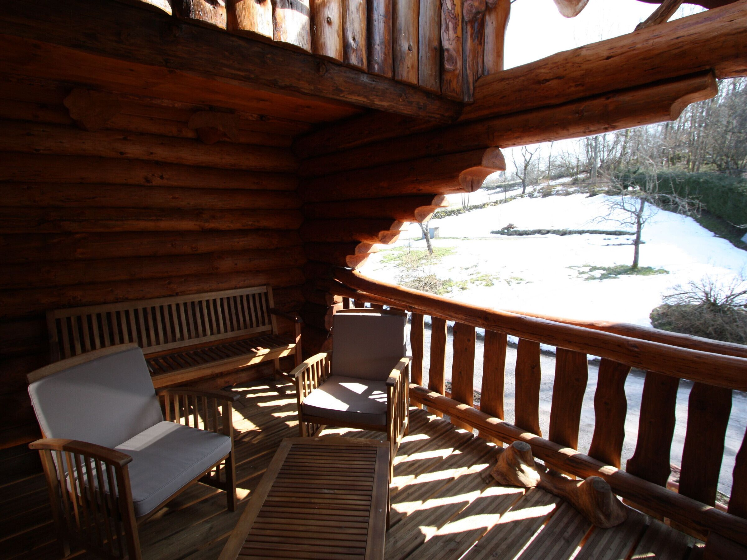 A wooden deck with a bench and chairs, overlooking a snowy landscape.