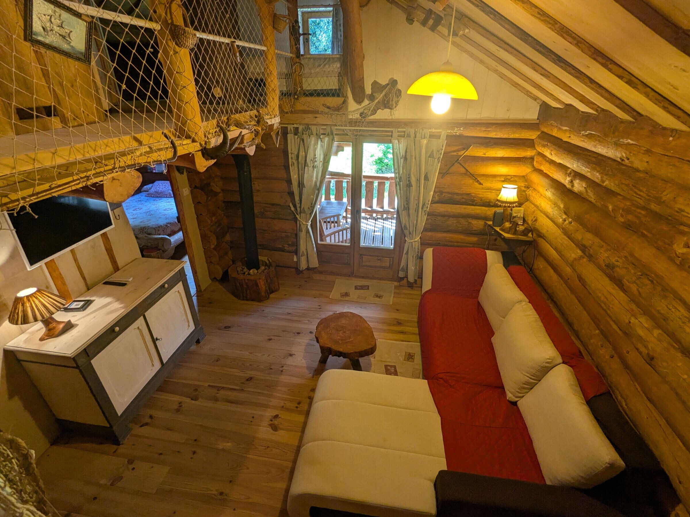 Un acogedor interior de cabaña de madera con un banco, una mesita con una lámpara y un sofá rojo y blanco.
