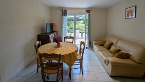 A dining area with a round table, chairs, a television, and a sofa. - Spacious Gîte: Fireplace, Terrace, Near Epinal & Gérardmer, Sleeps 5 (Docelles)