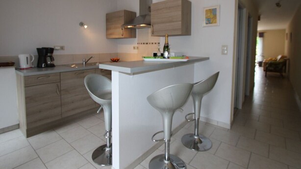 A modern kitchen with a central island, two bar stools, a coffee maker, and a bottle of champagne. - Spacious Gîte: Fireplace, Terrace, Near Epinal & Gérardmer, Sleeps 5 (Docelles)