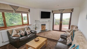 A living room with a fireplace, leather sofas, a wooden coffee table, and a TV mounted on the wall. - Oakland Cottage (Narberth)