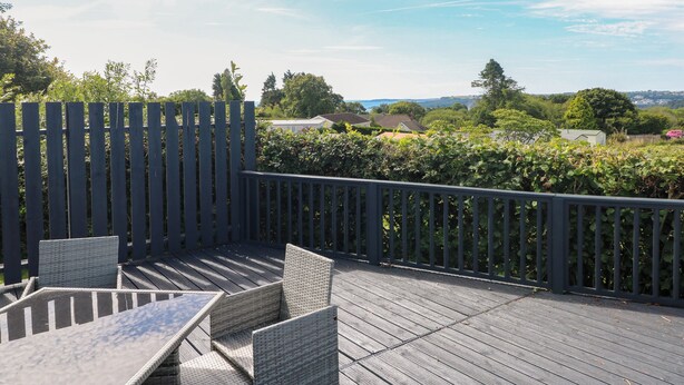 An outdoor deck with wicker furniture and a view of a residential area. - Oakland Cottage (Narberth)