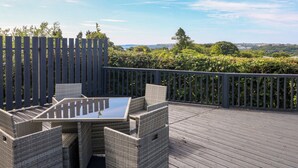 An outdoor deck with wicker furniture and a glass-top table, surrounded by a wooden fence and lush greenery. - Oakland Cottage (Narberth)