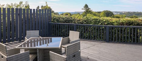 Eine Terrassenausstattung mit Korbmöbeln und einem Glastisch, umgeben von einem Holzzaun und üppiger Bepflanzung.