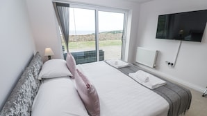 Une chambre d’hôtel avec un grand lit, un téléviseur fixé au mur et une vue sur l’extérieur grâce à une porte coulissante.