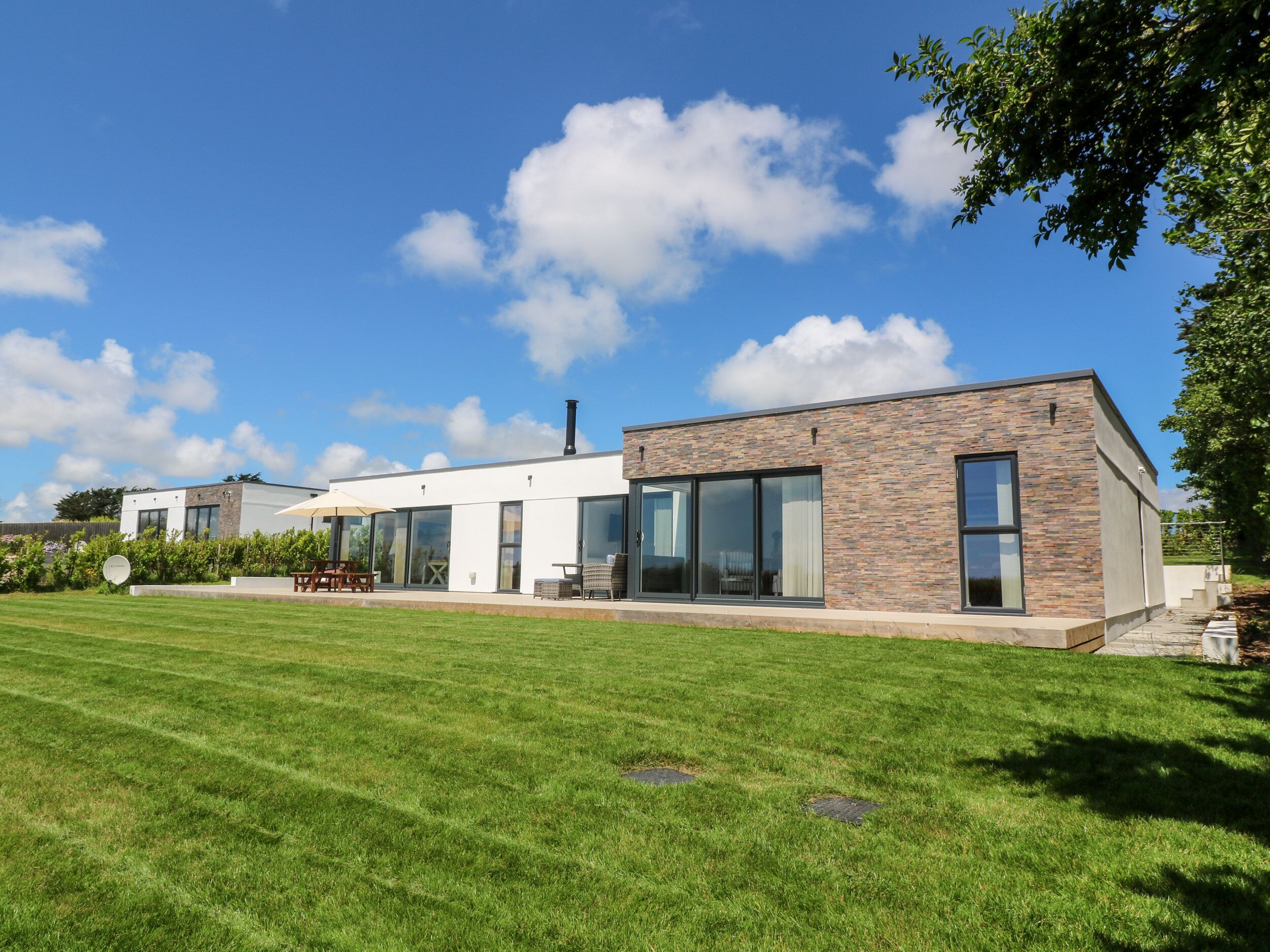 Een modern huis met een groot gazon, een terras met tuinmeubilair en een gevel van baksteen.