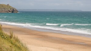 Une plage avec des vagues, une zone herbeuse et une falaise sur laquelle se trouve un bâtiment.