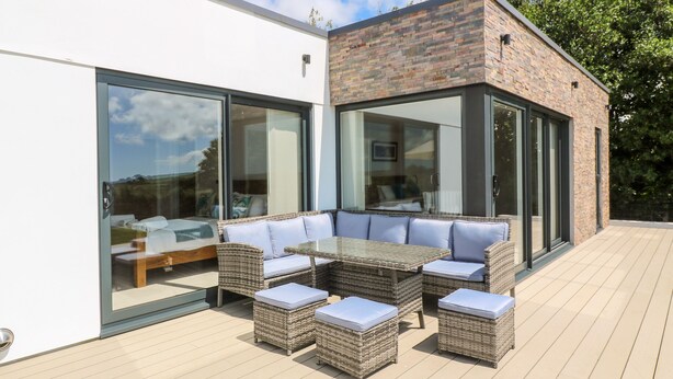 Une terrasse extérieure moderne, dotée de meubles en osier, de portes vitrées et d’un mur en briques.