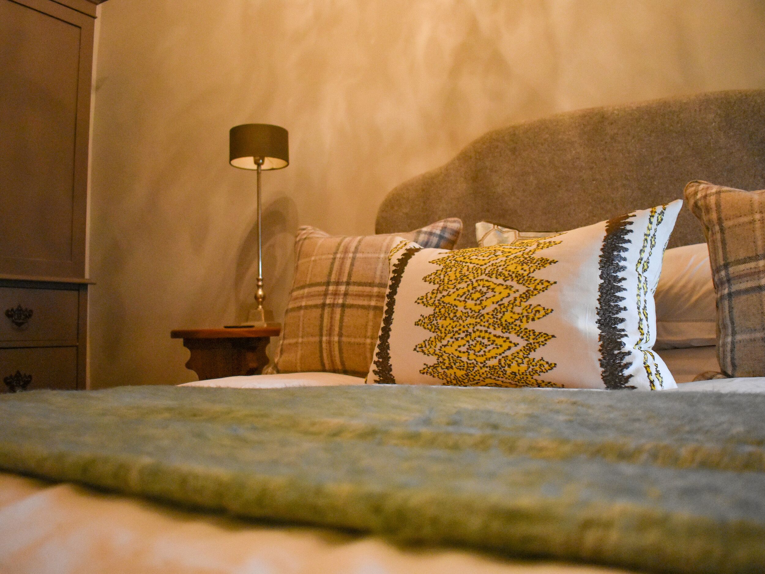 A neatly made bed with a plaid pillow and a decorative pillow with a geometric pattern.