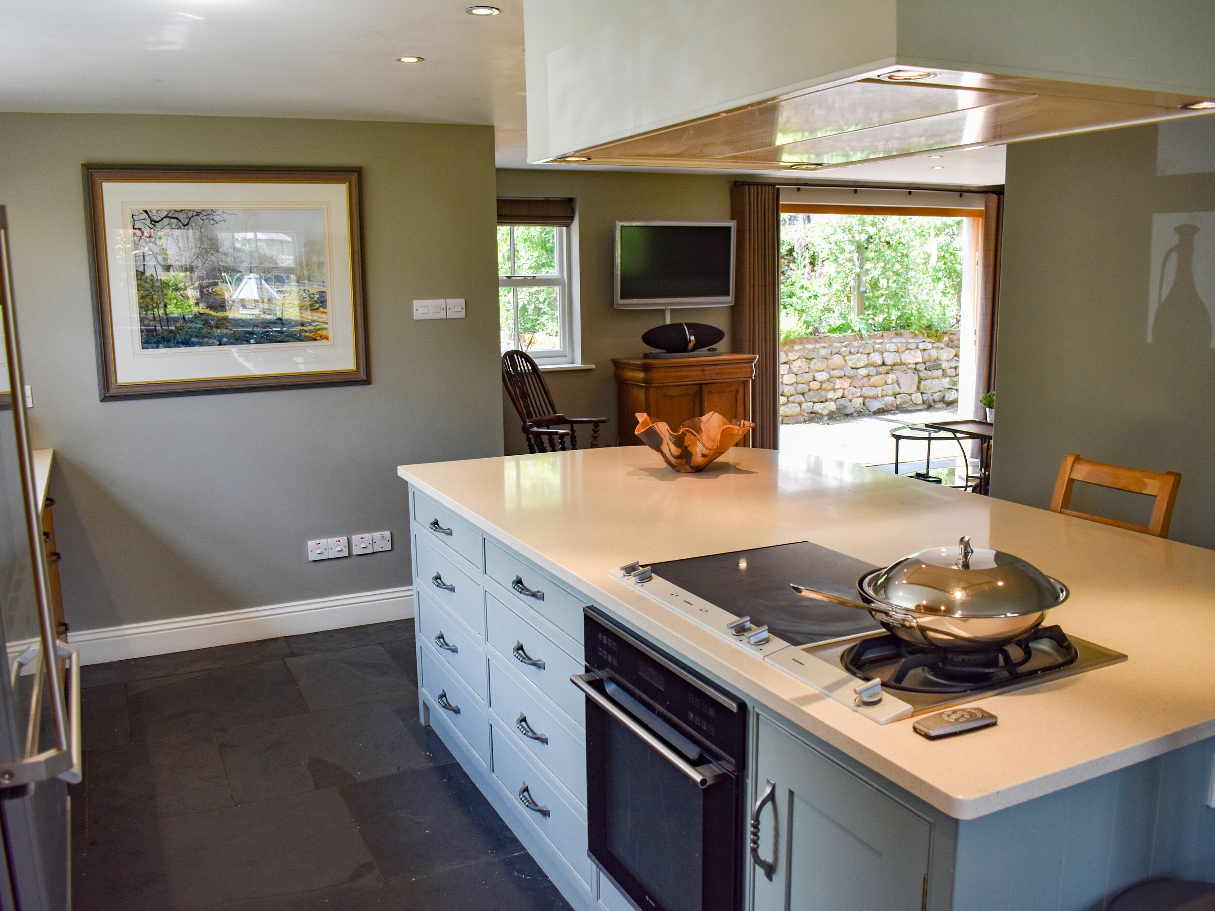 A modern kitchen with a central island, built-in oven, and a large window providing natural light.
