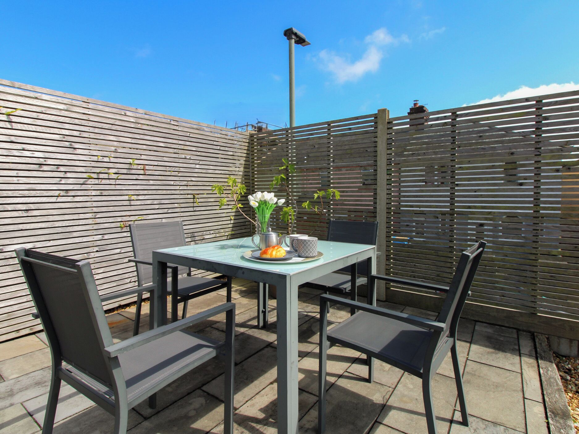 A patio with a table and chairs, a metal fence, and a street lamp.