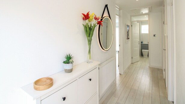 A hallway with a white radiator, a wooden bowl, a potted plant, and a mirror on the wall. - Little Starboard (Kingsbridge)