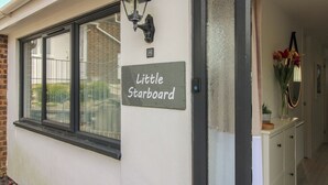 A building with a sign reading 'Little Starboard,' a black-framed window, and a white wall with a small number plaque. - Little Starboard (Kingsbridge)