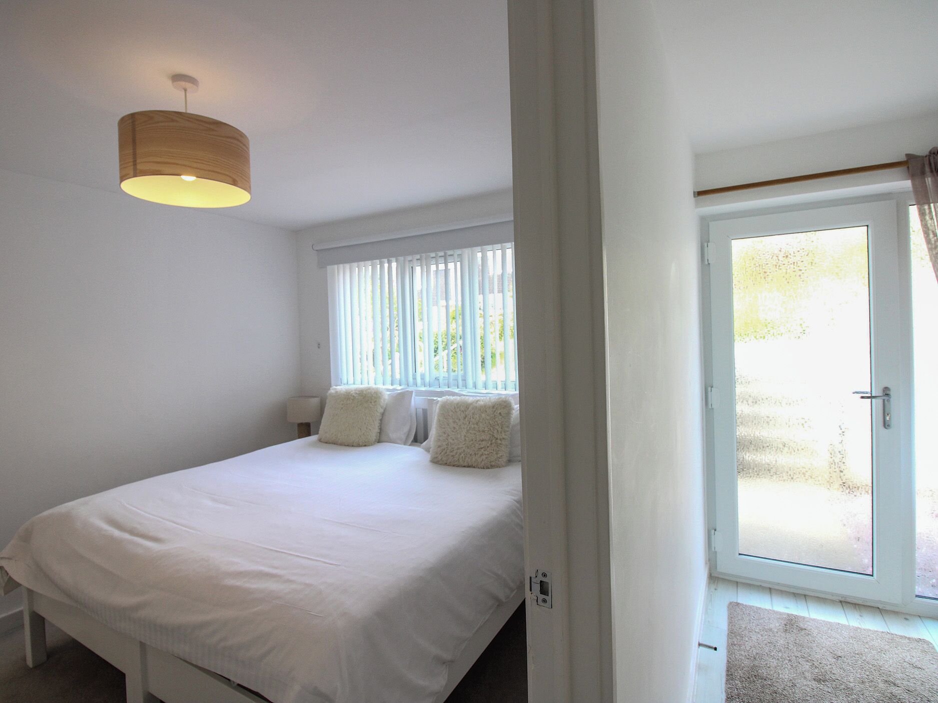 A bedroom with a bed, a window with blinds, a door leading outside, and a light fixture.