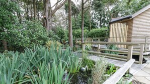 A serene garden with a pond, wooden bridge, and a wooden cabin. - Brambleside Lodge (Truro)
