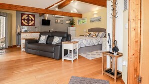 A cozy room with a sofa, a bed, a small table, and a wooden ceiling. - Brambleside Lodge (Truro)