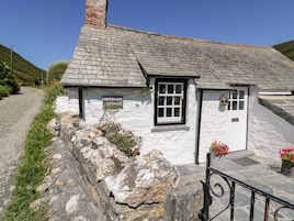 Una cabaña blanca con un muro de piedra y un letrero que dice 'Harbour Cottage'.