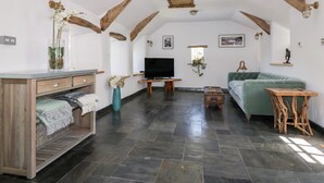 A spacious living area with exposed wooden beams, a flat-screen TV, a sofa, and a coffee table. - Harbour Cottage (Boscastle)