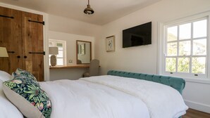 A bedroom with a bed, a wooden wardrobe, a desk, a chair, a television, and a window. - Harbour Cottage (Boscastle)