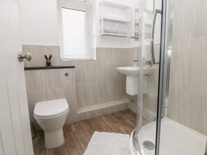 A modern bathroom with a toilet, sink, and glass-enclosed shower. - Hunters Cottage (High Peak)