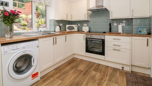 A compact kitchen with white cabinets, a built-in oven, a microwave, and a washing machine. - Hunters Cottage (High Peak)