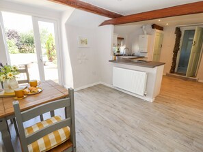 A bright kitchen with a wooden table and chairs, a radiator, and a view of the outdoors. - Ysgubor Ucha (Ruthin)